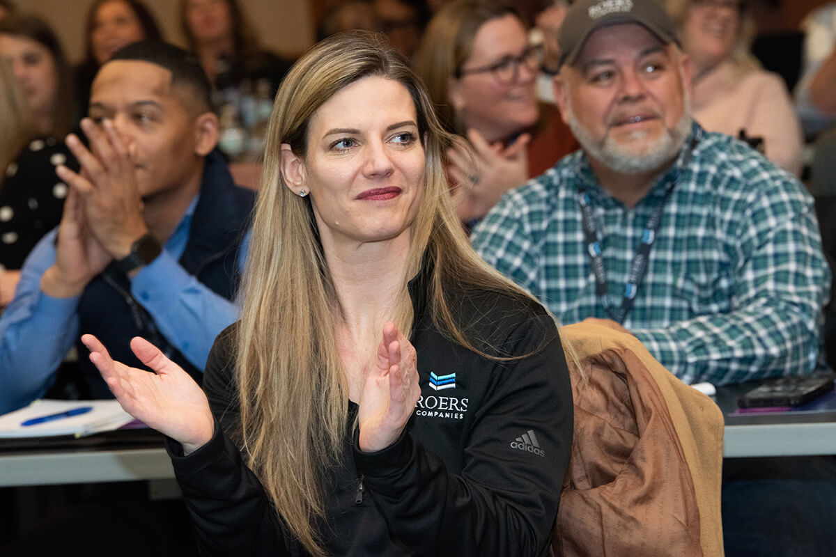 woman clapping at a conference, Roers Companies logo visible